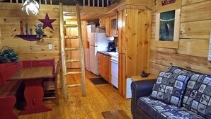 A cozy cabin interior with a wooden interior, a dining area with a red table and benches, a sofa with a patterned cover, and a kitchen with wooden cabinets and appliances. - Elk Cabin - 2 Bedroom/1 Bath Vacation Rental (Franklin)