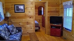 A cozy cabin interior with a wooden ceiling, a ceiling fan, a sofa, a TV, and a small table. - Elk Cabin - 2 Bedroom/1 Bath Vacation Rental (Franklin)