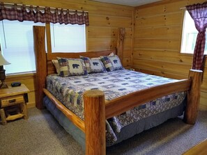 Quarto de cabana de madeira com cama, mesa de cabeceira e janela com cortinas.
