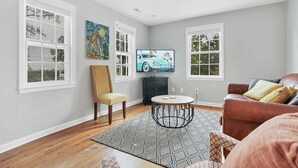 A living room with hardwood flooring, a round coffee table, a brown leather sofa, and a television on a stand. - HEART OF DOWNTOWN (Riverwalk, River View, Walk to Shopping, Dining, and Spirits) (Wilmington)