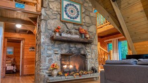 L’intérieur chaleureux d’un chalet avec une cheminée en pierre, des murs en bois et un coin salon confortable.