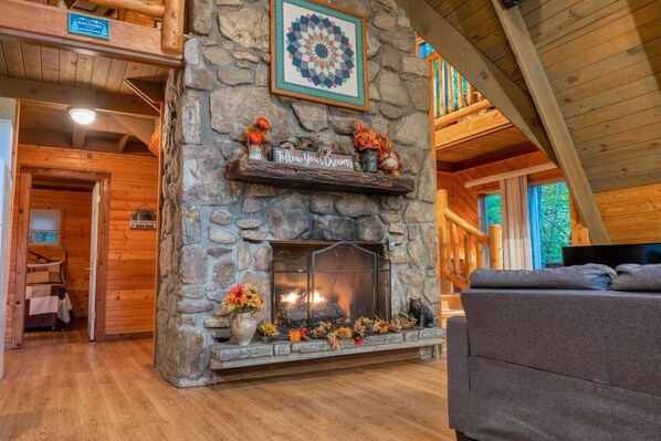 A cozy cabin interior with a stone fireplace, wooden walls, and a comfortable seating area.
