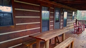 Une cabane en bois dotée d’un porche couvert, avec un long banc en bois et un fauteuil à bascule.
