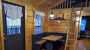 L’intérieur d’un chalet accueillant, avec une porte en bois sombre, un banc servant de siège, une petite table et une échelle.