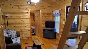 L’intérieur d’un chalet accueillant, avec un plancher en bois, un canapé, un banc, un meuble pour la télévision et une échelle.