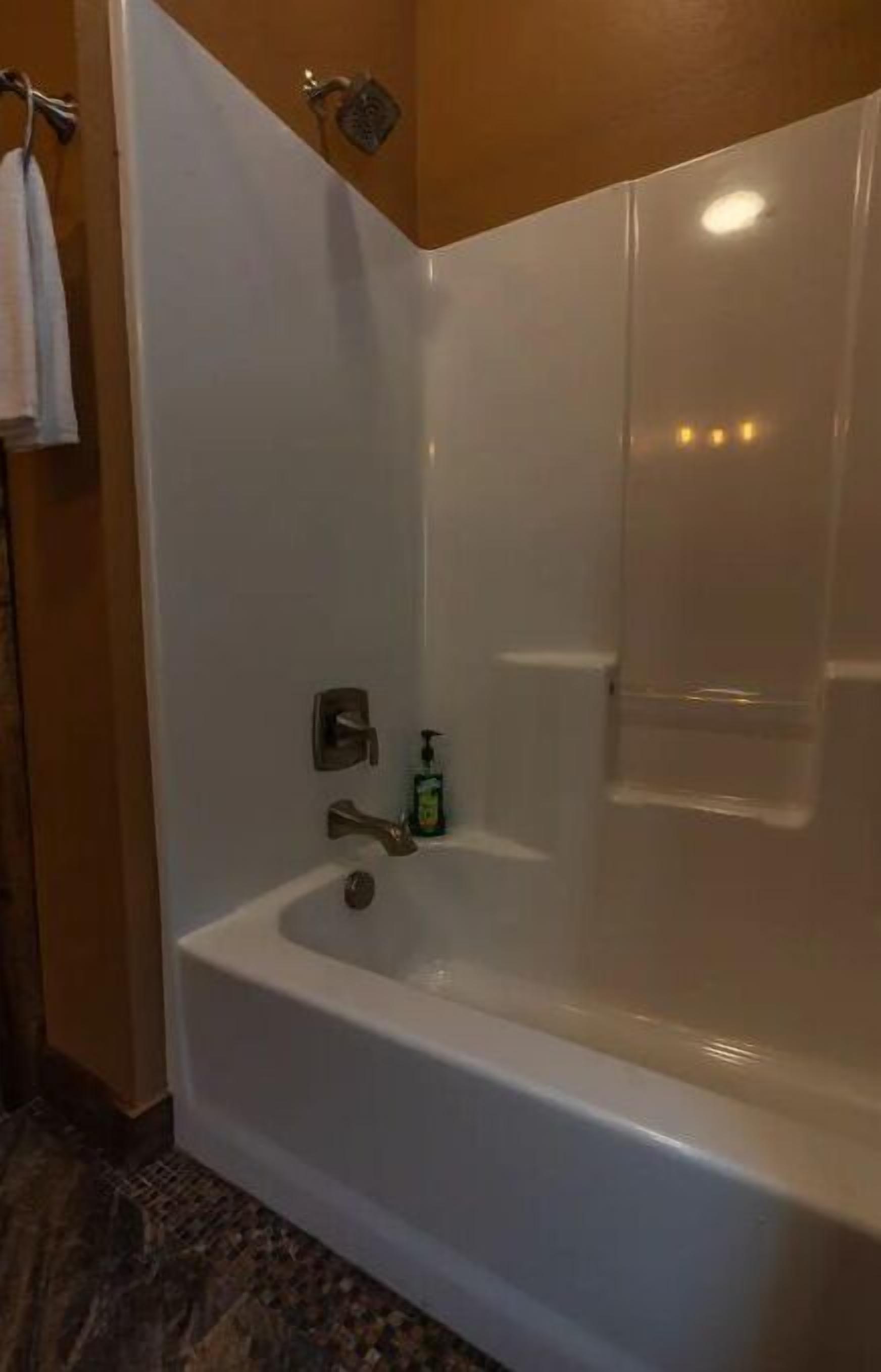 Un bagno moderno con una vasca da bagno bianca, un soffione a mano e una bottiglia di shampoo.