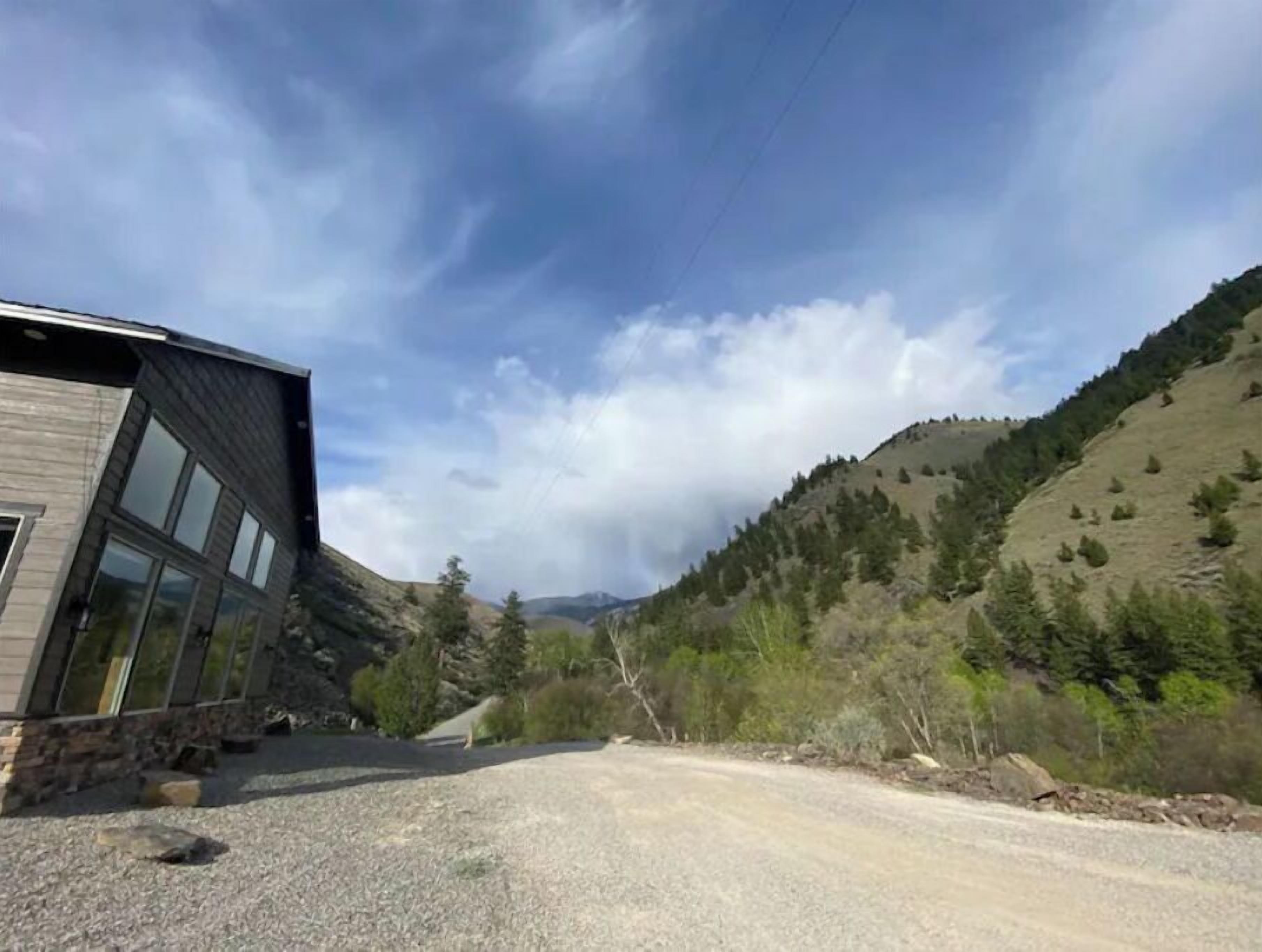 A modern building with large windows, a gravel driveway, and a mountainous landscape in the background.