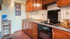 Une cuisine avec des meubles de rangement en bois, une cuisinière à gaz, une machine à café et un dosseret carrelé.