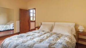 Une chambre à coucher avec un grand lit, une porte en bois, une fenêtre et une table de chevet avec une lampe.