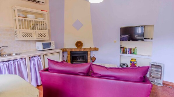 Un salon doté d’une cheminée, d’un téléviseur fixé au mur et d’un coin cuisine équipé d’un four à micro-ondes et de placards.