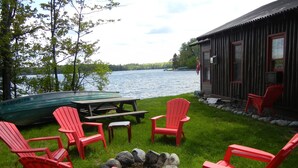 Una terrazza sul lago con poltroncine Adirondack rosse, un tavolo da picnic e un piccolo fuoco.