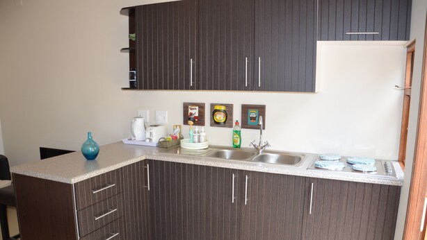 A kitchen with dark wood cabinets, a granite countertop, a sink, and a stove. - Sauvignon Country Lodge (Wellington)