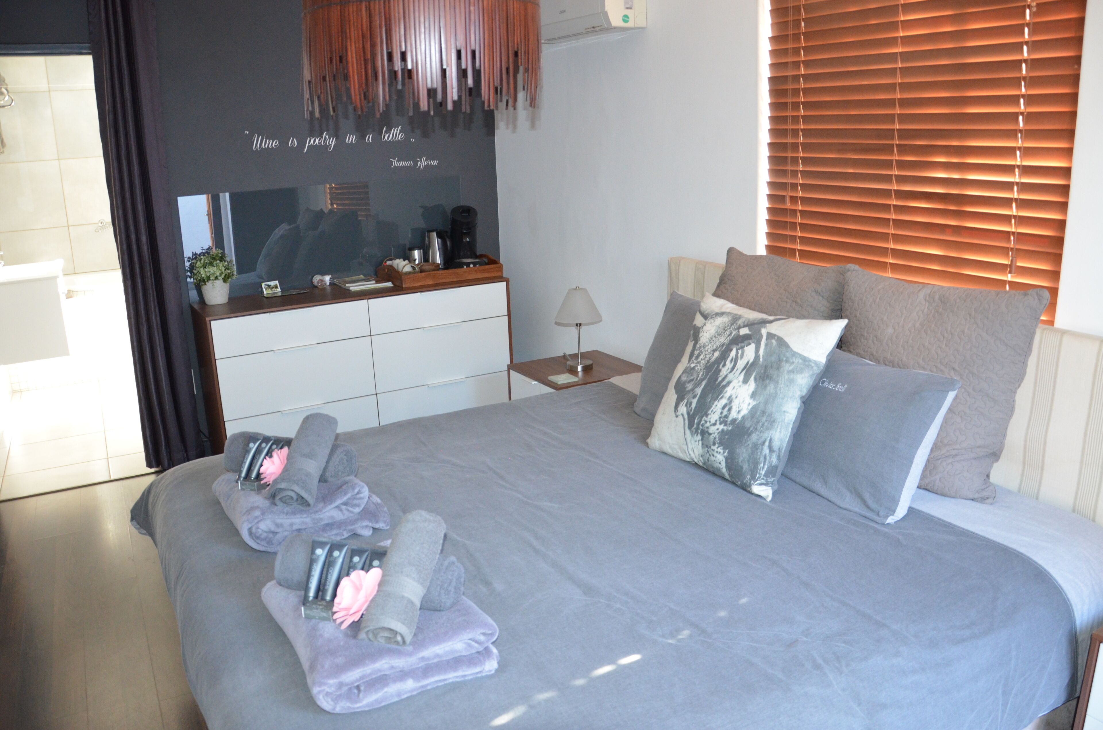 A neatly made bed with towels and toiletries, a bedside table with a lamp, and a wall with a quote.