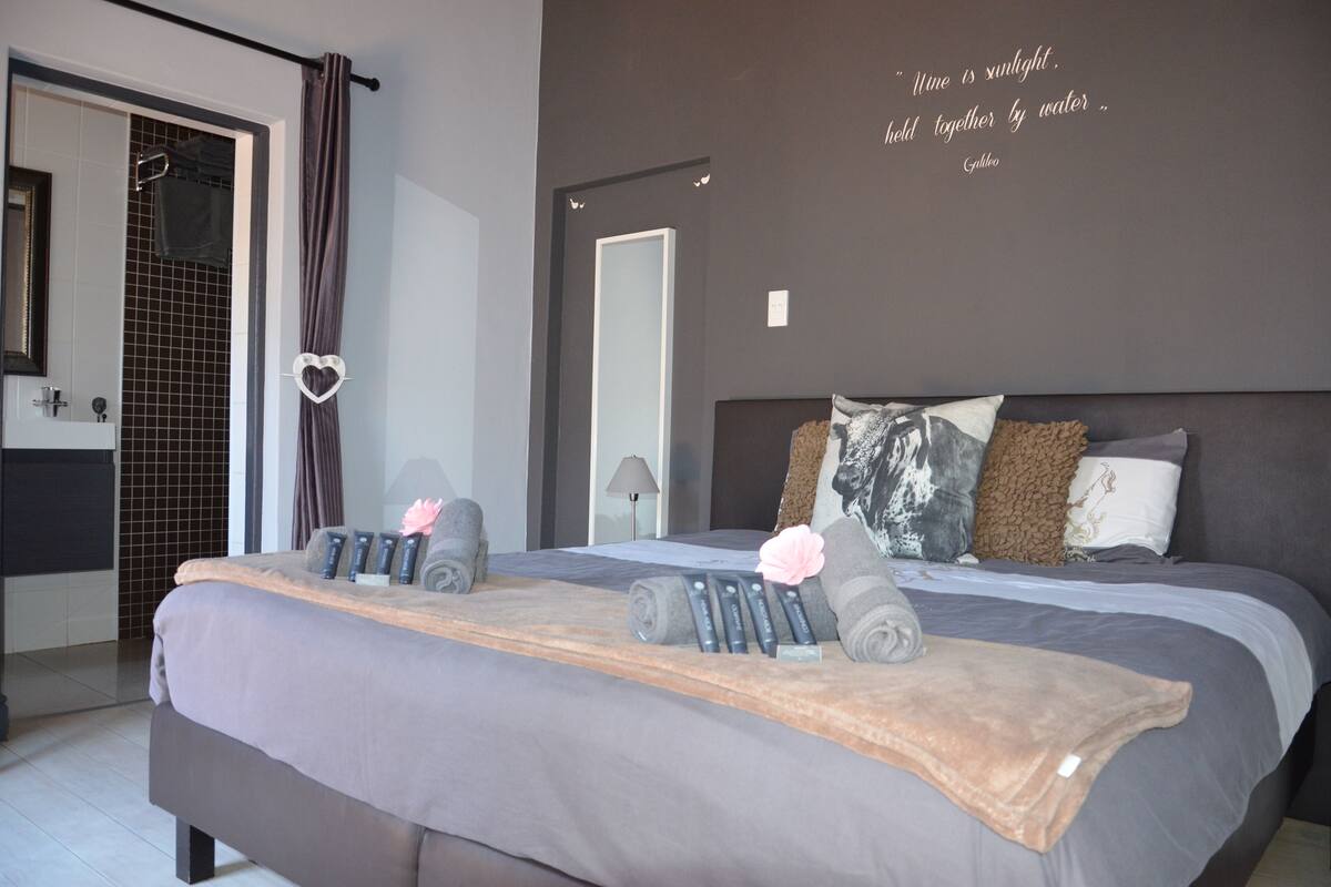 A modern bedroom with a large bed, a shower area, and a quote on the wall.