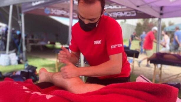 A person in a red shirt with "KEEP GOING" text, attending to someone lying on a red blanket under a purple canopy. - Sauvignon Country Lodge (Wellington)