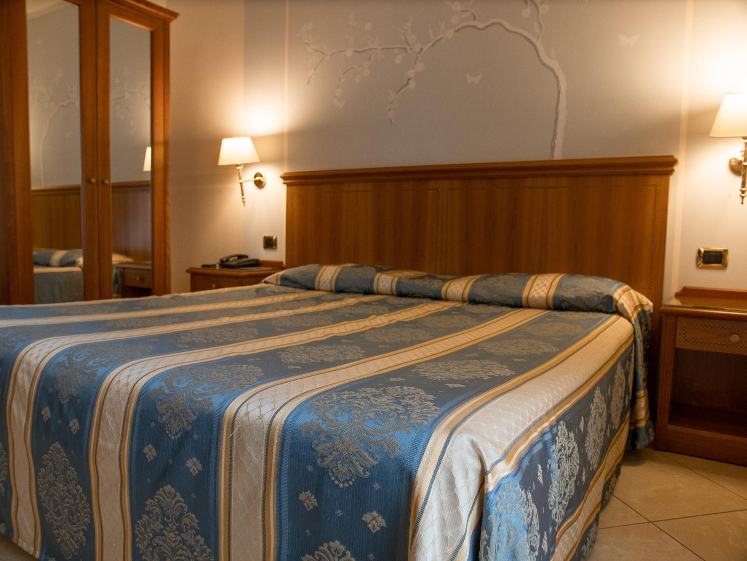Ein Hotelzimmer mit einem großen Bett, einem Holz-Kopfteil, zwei Nachttischen mit Lampen und einem Spiegel an einer Wand.