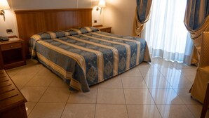 Une chambre d’hôtel avec un grand lit, une tête de lit en bois, deux tables de chevet, un bureau et une lampe.