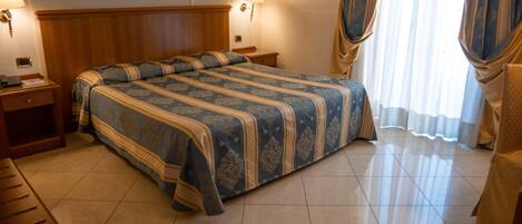 Habitación de hotel con una cama grande, cabecera de madera, dos mesitas de noche, un escritorio y una lámpara.