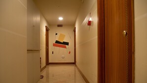 Un couloir avec un sol carrelé, une porte en bois sur la droite et un mur orné d’œuvres d’art abstraites.