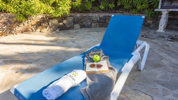 A sun lounger with a towel, an apple, a book, and sunglasses.