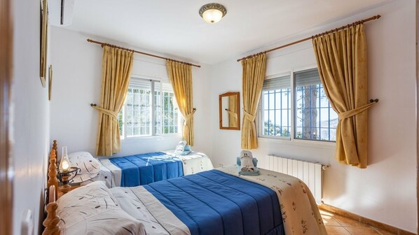 Ein Schlafzimmer mit zwei Betten, einem Nachttisch, einer Lampe und einem Fenster mit Vorhängen.