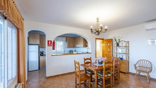Ein Essbereich mit Holztisch und -stühlen, einer Chandelüster und Blick in die Küche.
