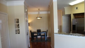 A modern kitchen with a stainless steel refrigerator, a dining area with a table and chairs, and a hallway with a door and wall decorations.