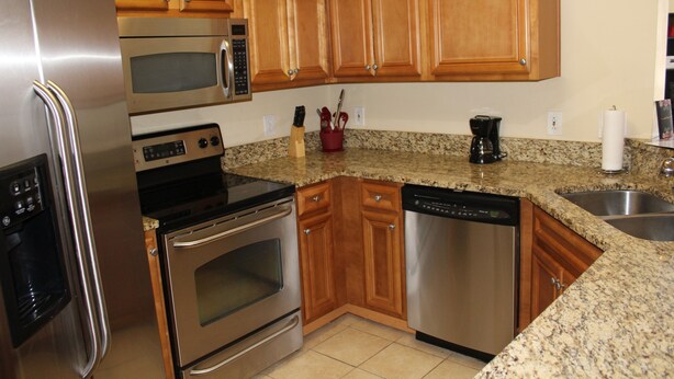 A kitchen with wooden cabinets, stainless steel appliances including a refrigerator, microwave, oven, and dishwasher, granite countertops, and a coffee maker.
