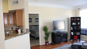 A compact living space with a kitchenette, a television, a bookshelf, and a potted plant.