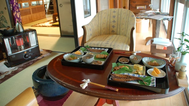 Una habitación japonesa tradicional con suelo de tatami, una mesa baja con una bandeja de sushi, una silla y un armario de madera.
