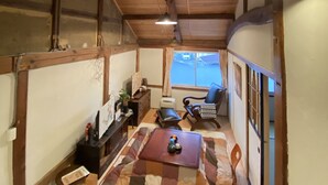 Un pasillo estrecho con vigas de madera, una mesa de comedor con mantel a cuadros, un sofá y una silla.