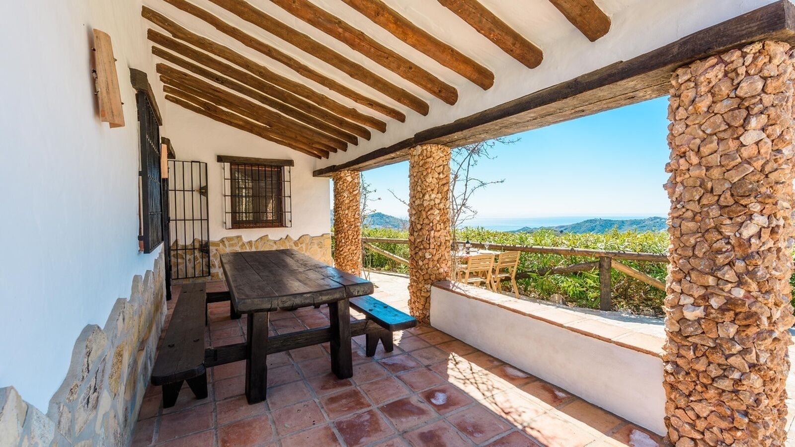 A patio with a wooden table and chairs, stone pillars, and a view of the landscape.
