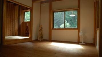 Una habitación con piso de madera, un ventanal con vista a árboles y un ventilador.