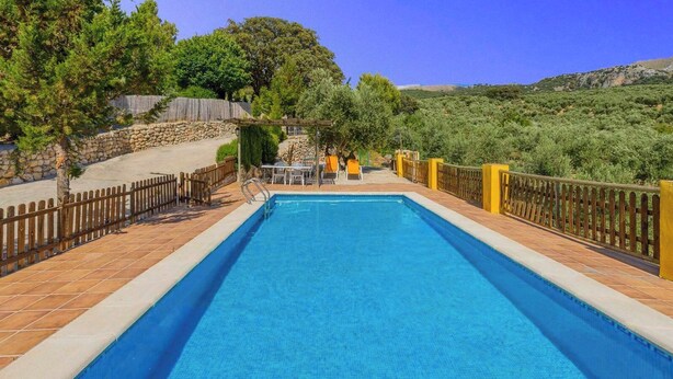 Une piscine rectangulaire avec une terrasse carrelée, entourée d’une clôture en bois et de piliers jaunes.