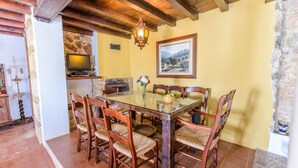 Un comedor con mesa de vidrio, sillas de madera, chimenea de piedra y candelabro.