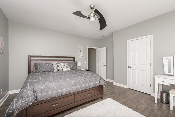 A bedroom with a bed, a ceiling fan, a white door, and a small white desk. - The Cycle Inn - on the Monon Trail Downtown Indy (Indianapolis)