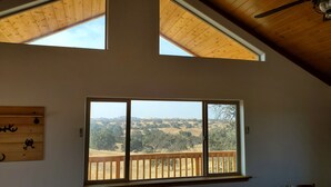 Ein Zimmer mit einer großen Glasschiebetür, die auf einen Balkon mit Holzgeländer führt. Das Zimmer besitzt eine schräge Decke mit Holzbalken und einem Oberlicht.