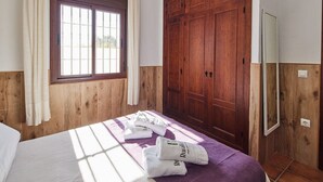 A bedroom with a wooden wardrobe, a bed with a purple blanket, and a window with curtains. - Chalet El Cancelín Conil de la Frontera by Ruralidays (Cádiz)