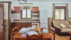 A dining area with a wooden table set for four, a kitchen with a refrigerator, and a living area with a sofa. - Chalet El Cancelín Conil de la Frontera by Ruralidays (Cádiz)