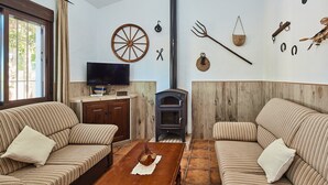 A cozy living room with striped sofas, a wooden coffee table, a television, and a wood-burning stove. - Chalet El Cancelín Conil de la Frontera by Ruralidays (Cádiz)