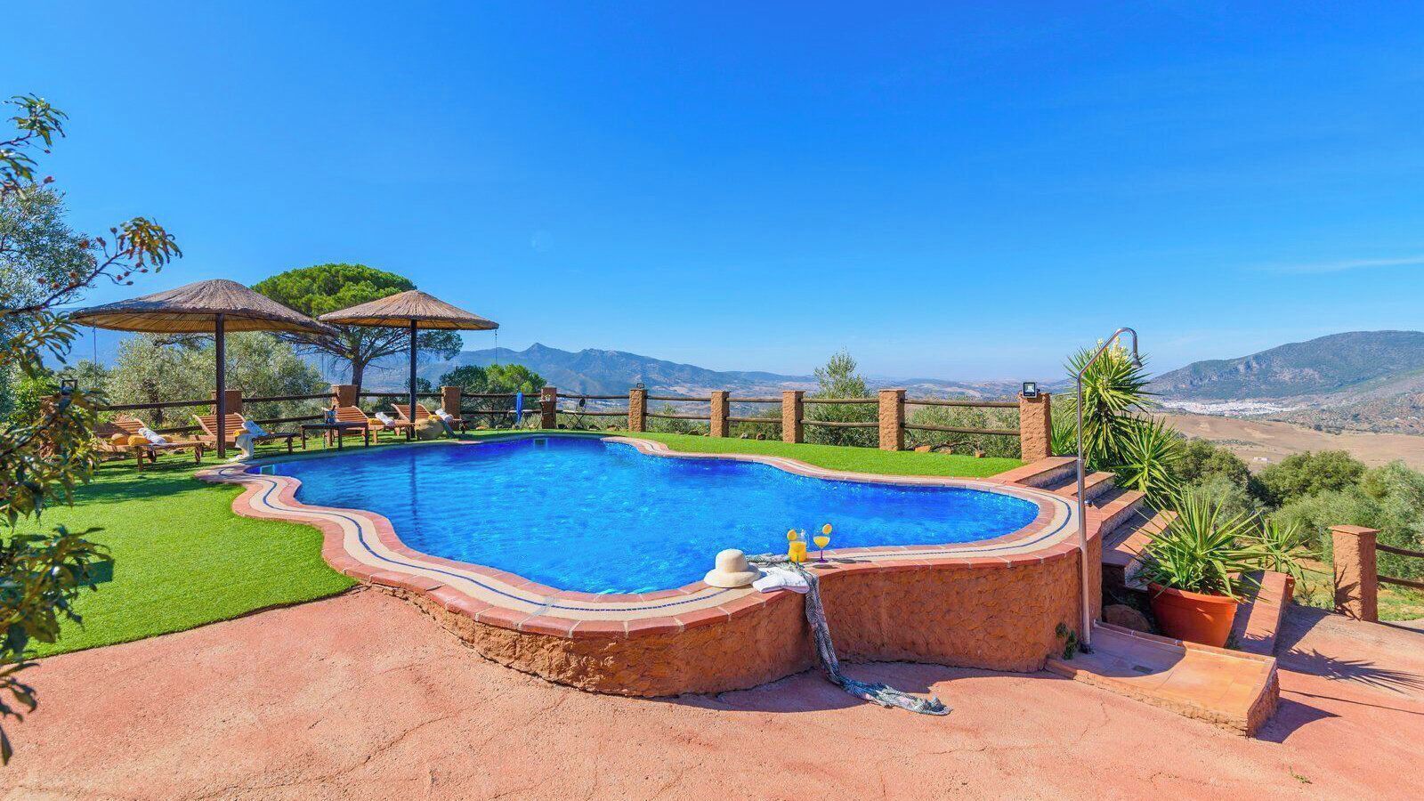 A swimming pool with a curved edge, surrounded by a brick deck and a wooden fence.