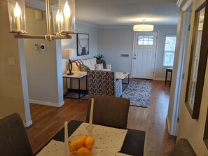 A dining area with a table set for two, a vase of oranges, and a patterned rug.