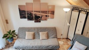 Een woonkamer met een grijze bank, een bijzettafeltje, een vloerlamp en een muur met een zonsondergangschilderij.