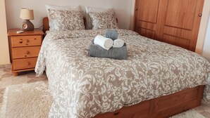 Een slaapkamer met een bed, een nachtkastje van hout, een lamp, een schilderij aan de muur en een houten deur.
