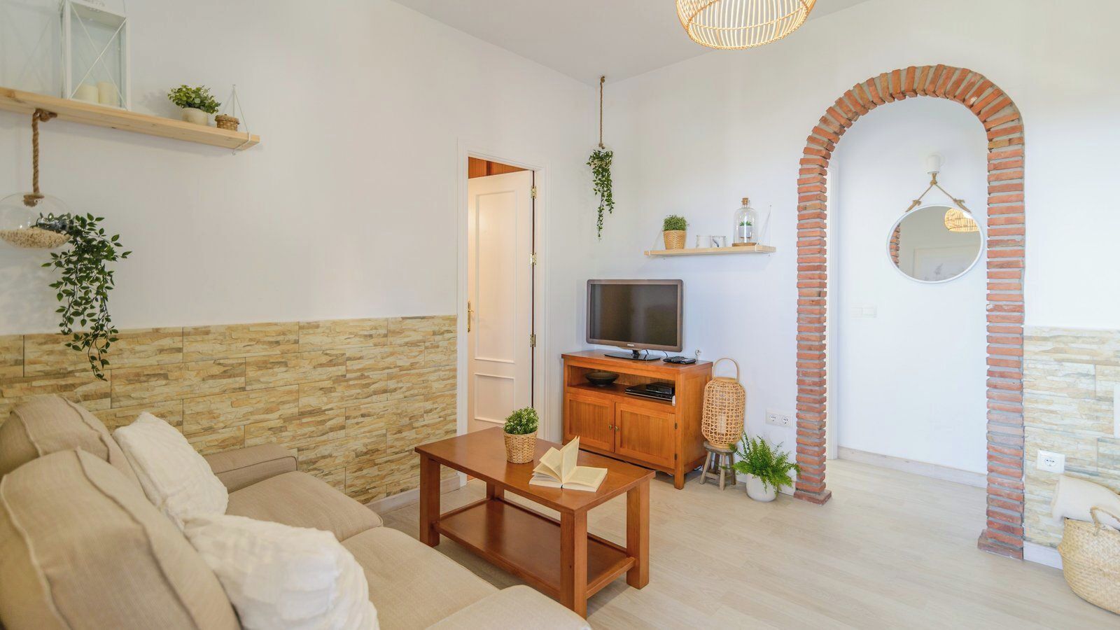 Un salon avec un canapé, une table basse en bois, un téléviseur et une arche en briques.
