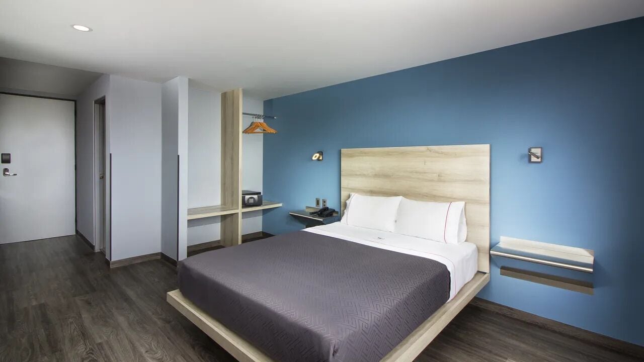 A modern hotel room with a large bed, a wooden headboard, a bedside table, and a wardrobe.