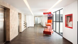 A modern hotel corridor with marble walls, wooden flooring, and a red seating area. - Hotel MX lagunilla CDMX, Trademark Collection by Wyndham (Mexico City)