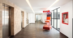 Un couloir d’hôtel moderne avec des murs en marbre, un plancher en bois et un espace détente rouge.