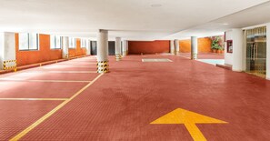 A spacious indoor parking area with red-tiled flooring, directional arrows, and concrete pillars with caution tape. - Hotel MX lagunilla CDMX, Trademark Collection by Wyndham (Mexico City)