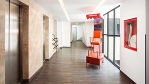 A modern hotel corridor with marble walls, a wooden floor, and a red seating area. - Hotel MX lagunilla CDMX, Trademark Collection by Wyndham (Mexico City)